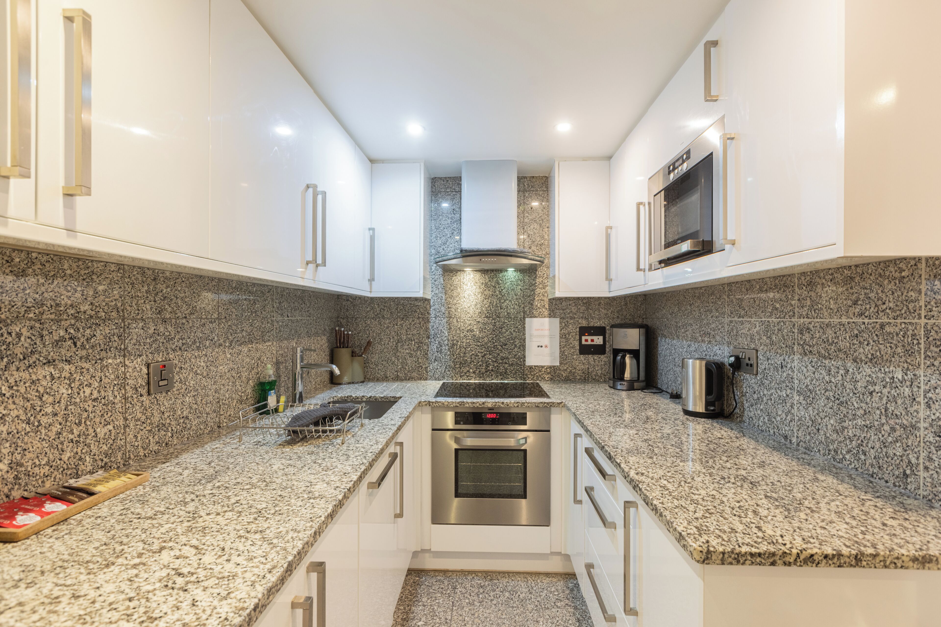 A modern kitchen with granite countertops, stainless steel appliances, and white cabinetry.