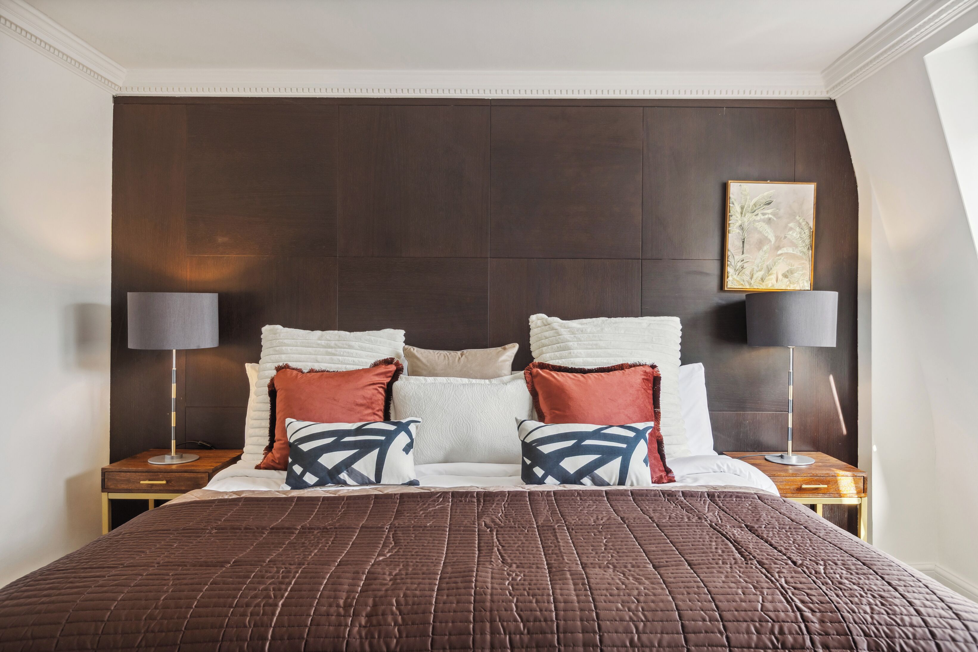 A neatly made bed with a brown quilt, a dark headboard, and two bedside tables with lamps.