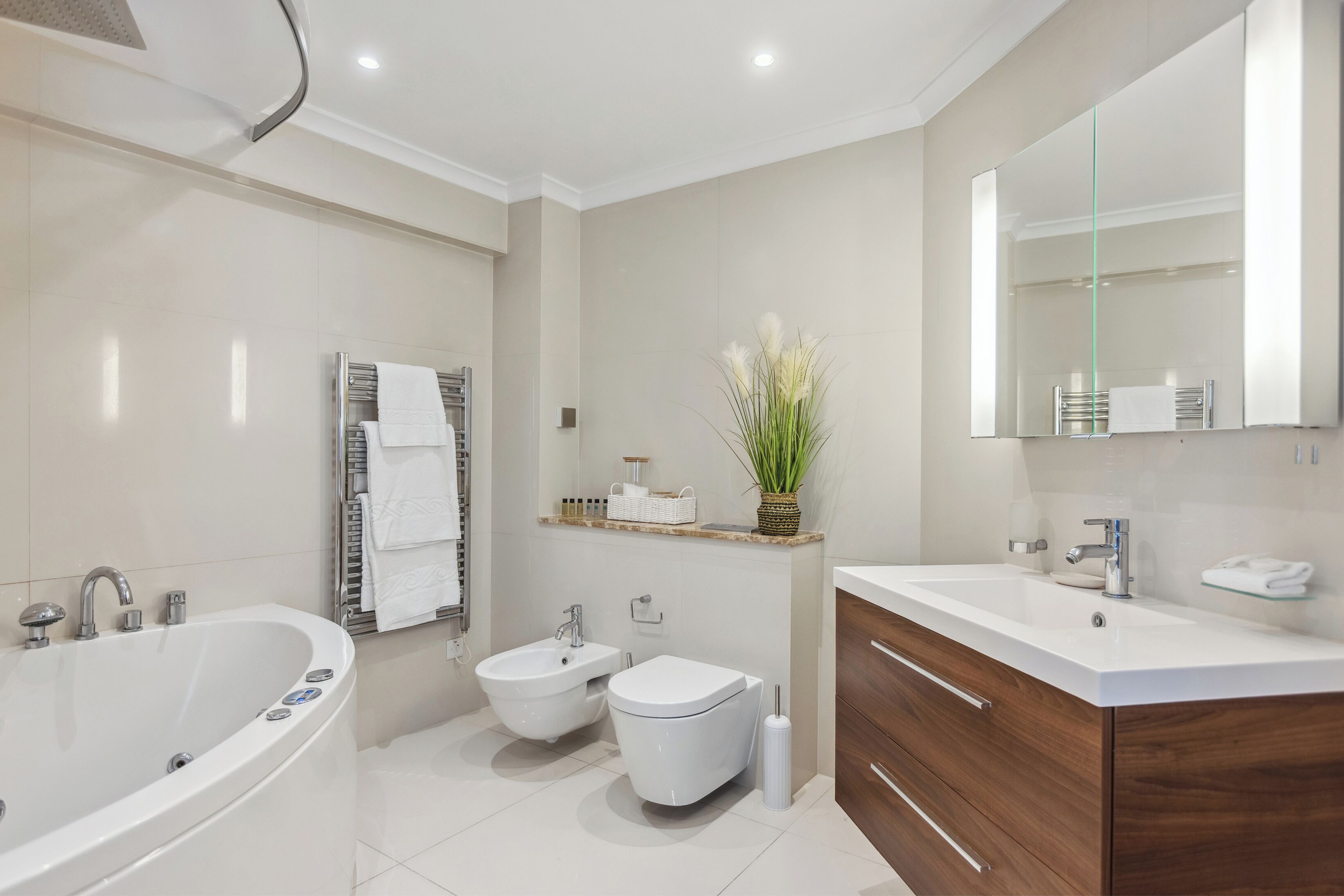 A modern bathroom with a freestanding bathtub, a bidet, a toilet, and a vanity with a mirror.