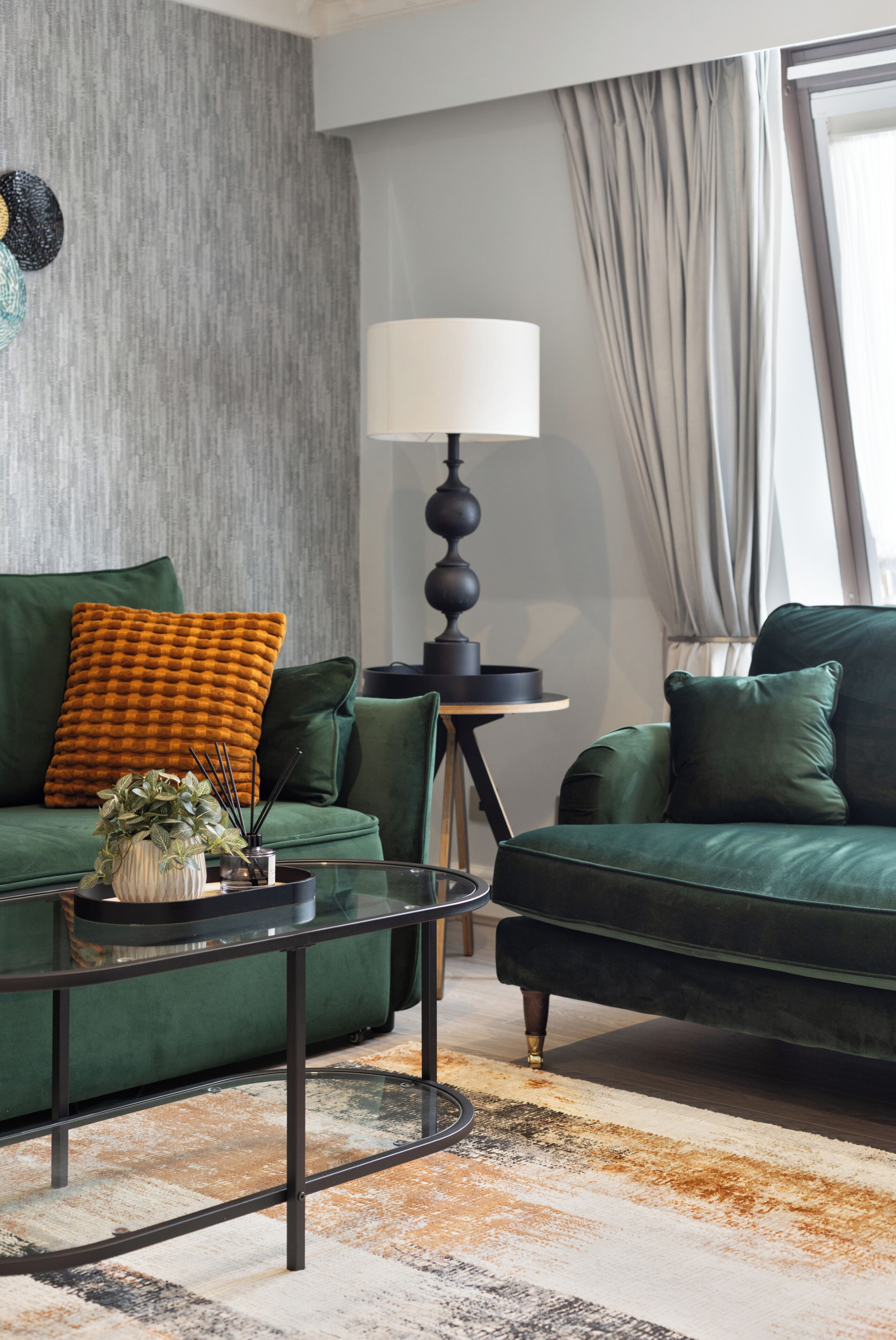 A modern living room with a green sofa set, a glass coffee table, a floor lamp, and a patterned rug.
