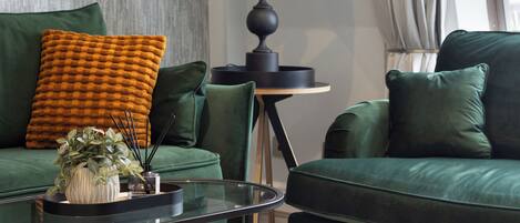 A modern living room with a green sofa set, a glass coffee table, a floor lamp, and a patterned rug.