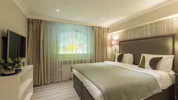 A hotel room with a large bed, a flat-screen TV, a potted plant, and a window with curtains.