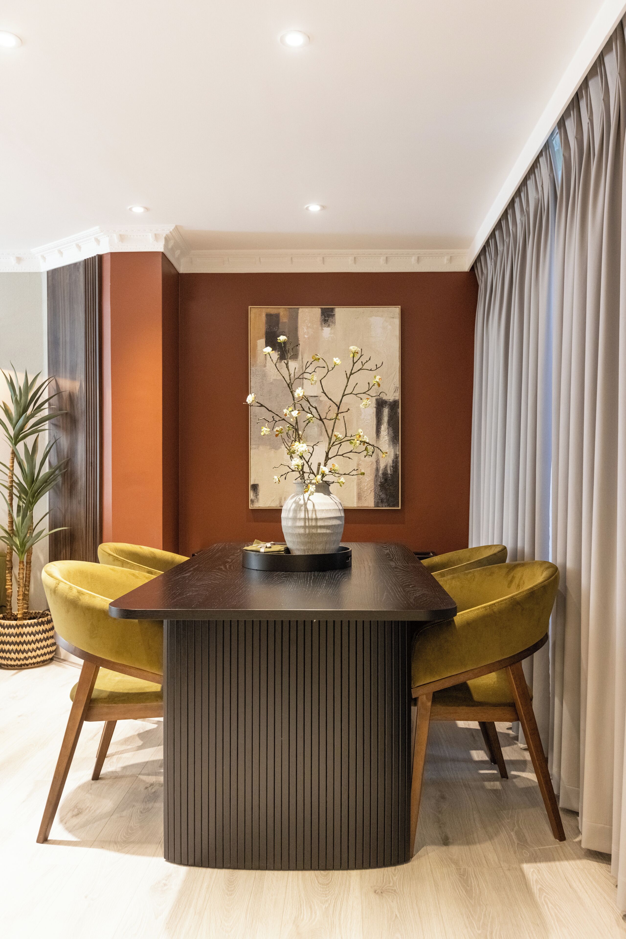 Un comedor con una mesa de madera oscura, dos sillas amarillas, un florero con flores y un cuadro abstracto grande en la pared.