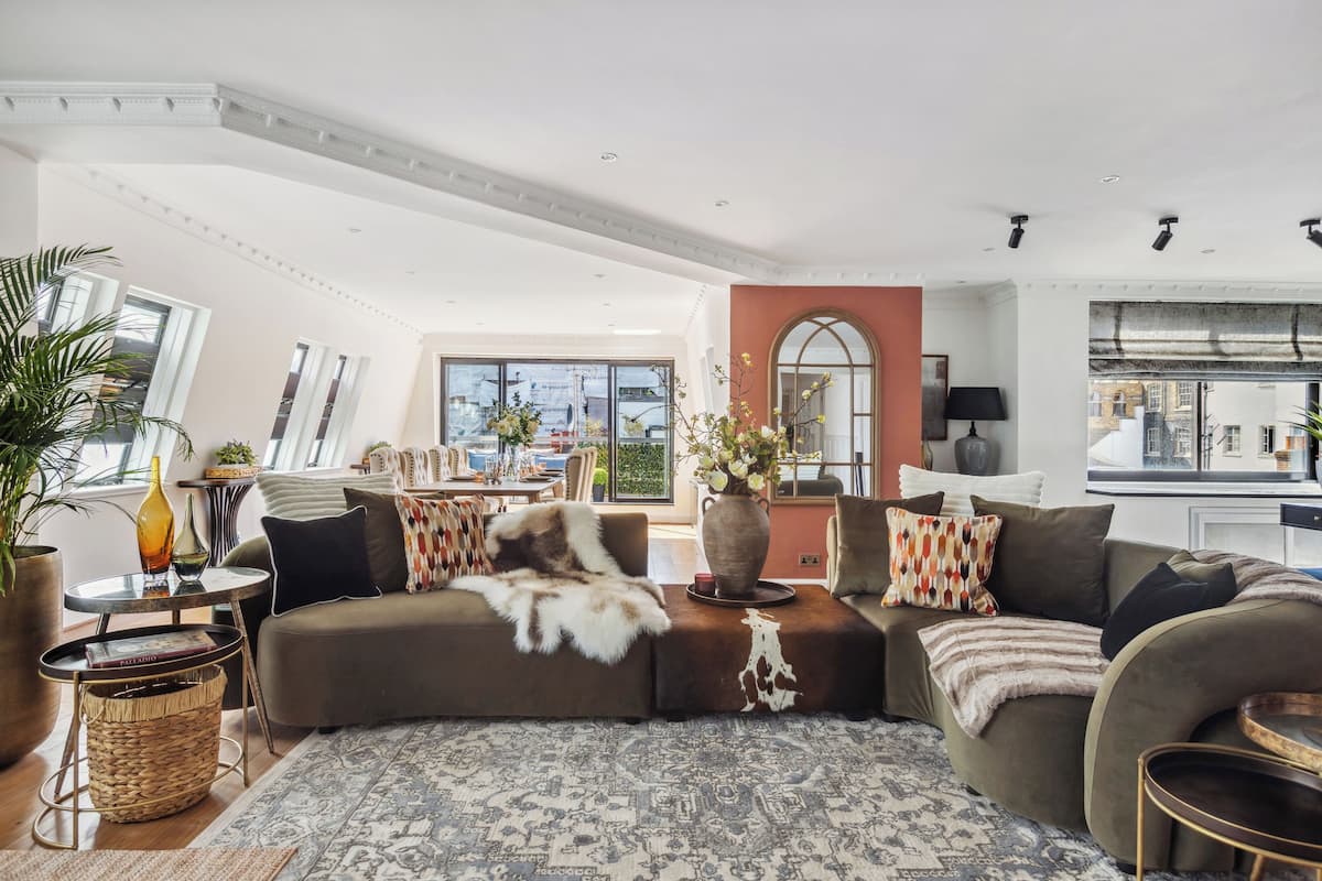 A spacious living room with a large sofa, a coffee table, and a view of the city through large windows.