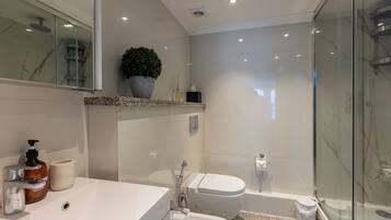 A modern bathroom with a large mirror, a sink, a bidet, a shower, and a potted plant.
