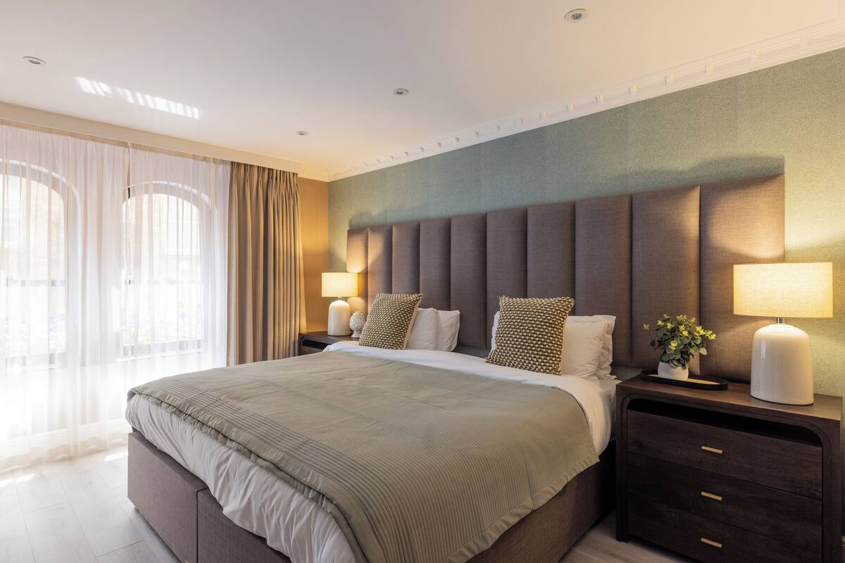 A modern hotel room with a large bed, two bedside tables, a nightstand, and a view of the outdoors.