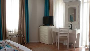 Habitación de hotel con cama, escritorio, silla, televisor y radiador.