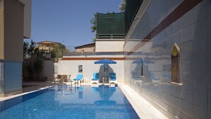 A swimming pool with blue tiles, lounge chairs, and a sun umbrella. - Nasa Flora Hotel (Antalya)