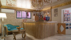 A reception area with a reception desk, a blue sofa, a small table, and a chandelier. - Nasa Flora Hotel (Antalya)