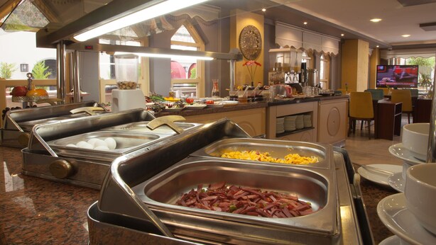 A buffet area with multiple food stations, including a ham station, a cheese station, and a fruit station. - Nasa Flora Hotel (Antalya)