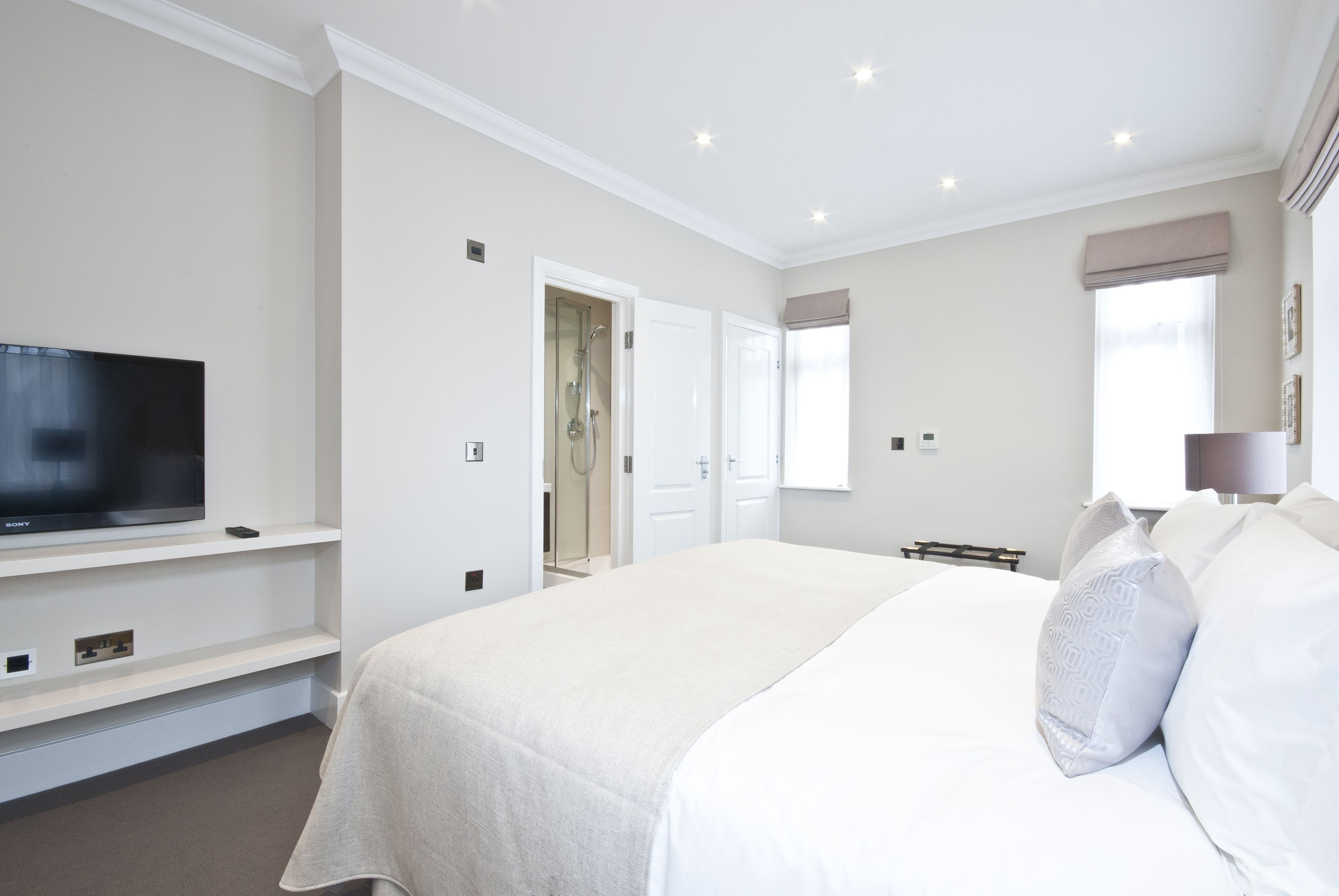 Ein Hotelzimmer mit einem großen Bett, einem Fernseher auf einem Tisch, einer Dusche und einem Fenster mit Vorhängen.
