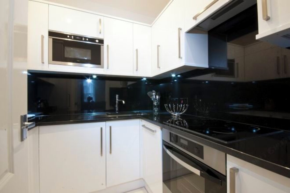 A modern kitchen with white cabinets, a black countertop, stainless steel appliances, and under-cabinet lighting.