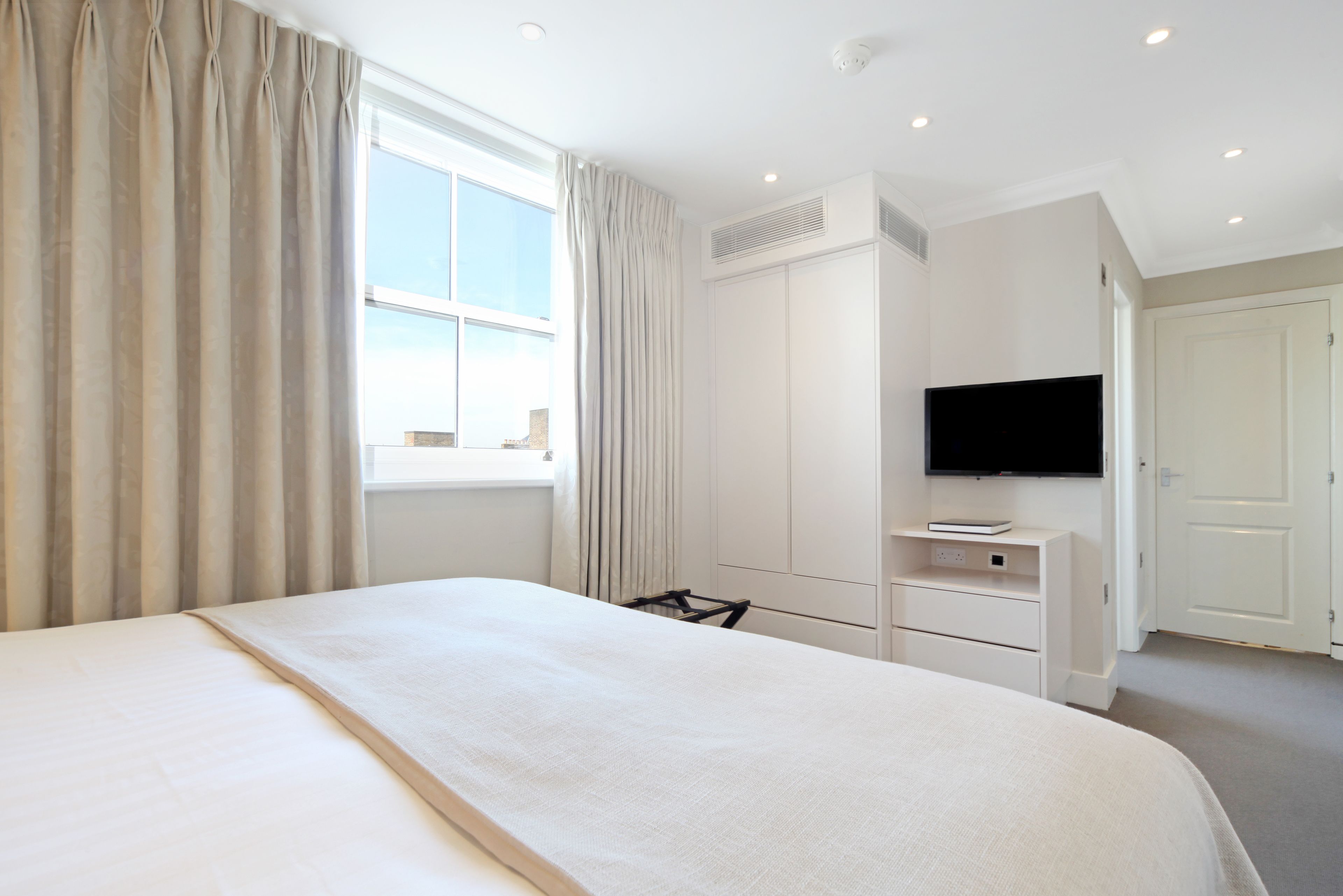 A hotel room with a large bed, a TV mounted on the wall, a desk with a chair, and a wardrobe.
