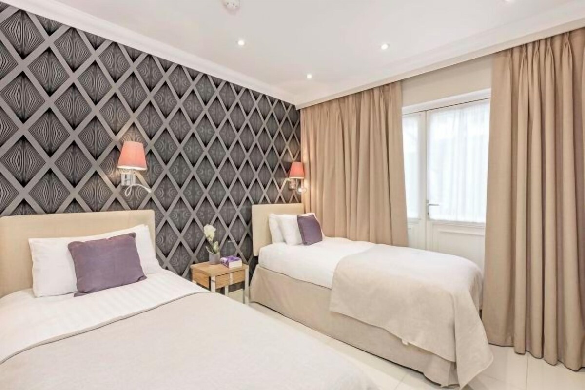 A hotel room with two beds, a patterned wall, and a window with curtains.