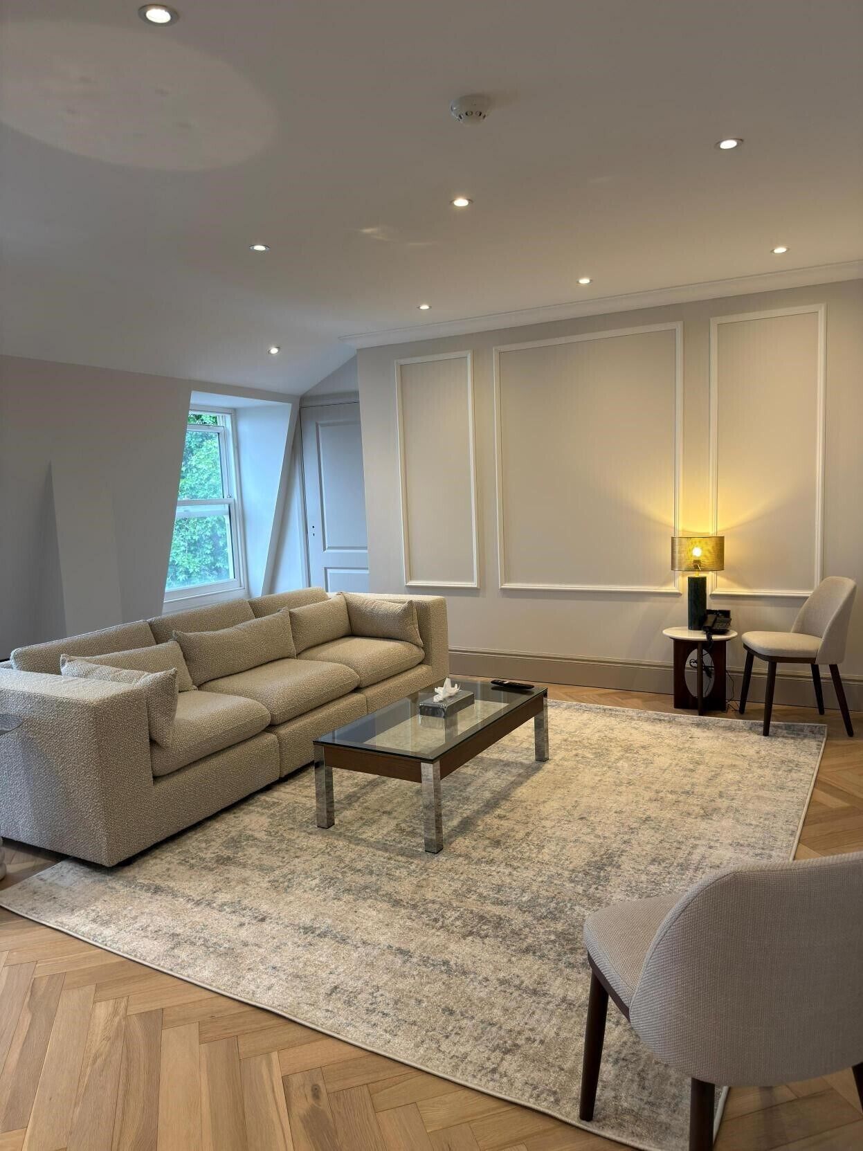 A modern living room with a sectional sofa, a glass coffee table, a rug, a lamp, and a chair.