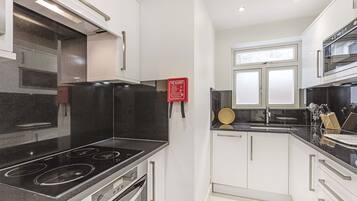 A modern kitchen with a black stove, white cabinets, and a red fire safety sign.