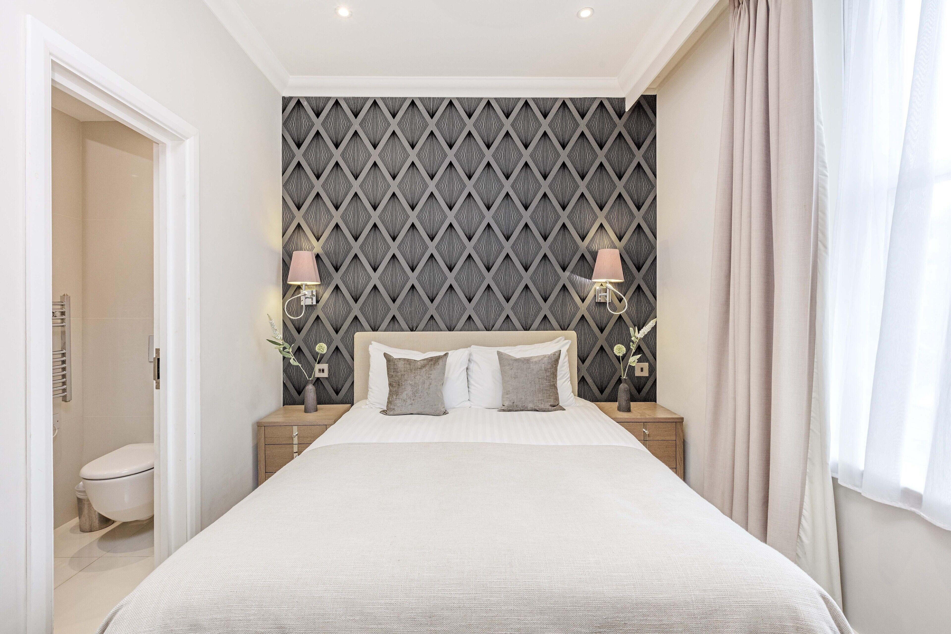A neatly arranged bedroom with a large bed, two bedside tables, and a headboard with a geometric pattern.