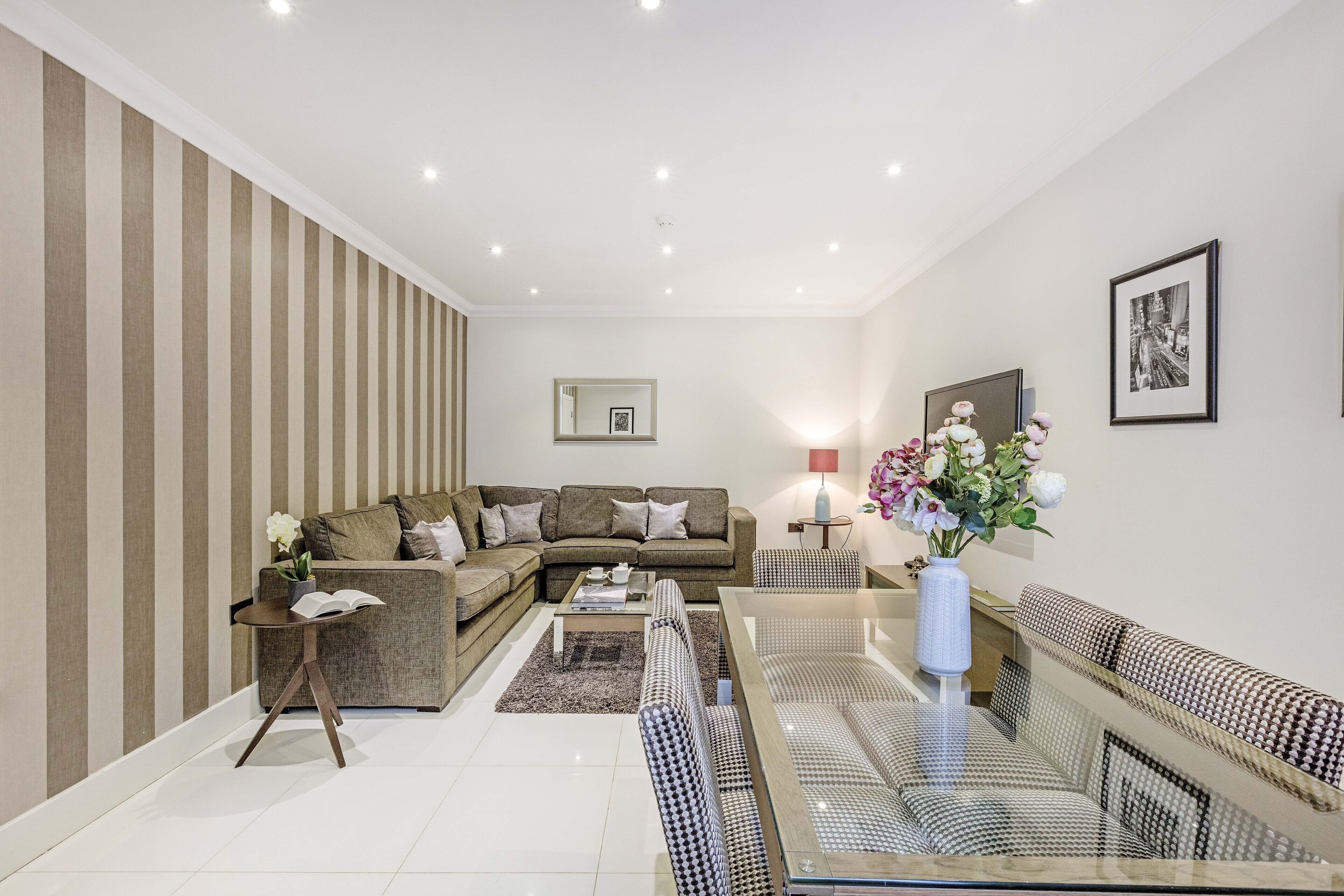 Uma sala de estar moderna com um sofá modular, uma mesa de centro de vidro e uma parede listrada.