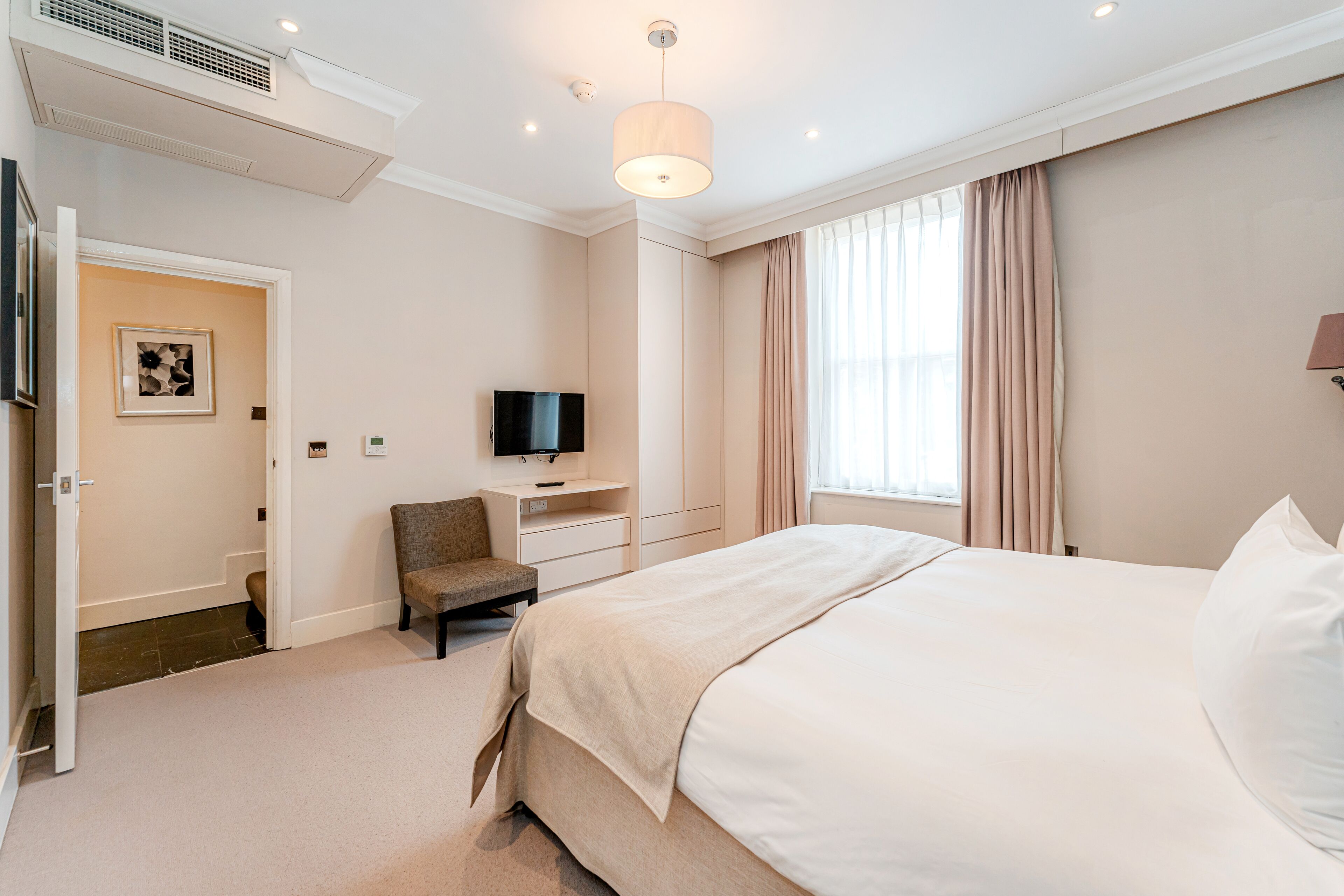 Une chambre d’hôtel avec un lit, une chaise, une télévision, un bureau et une fenêtre avec des rideaux.