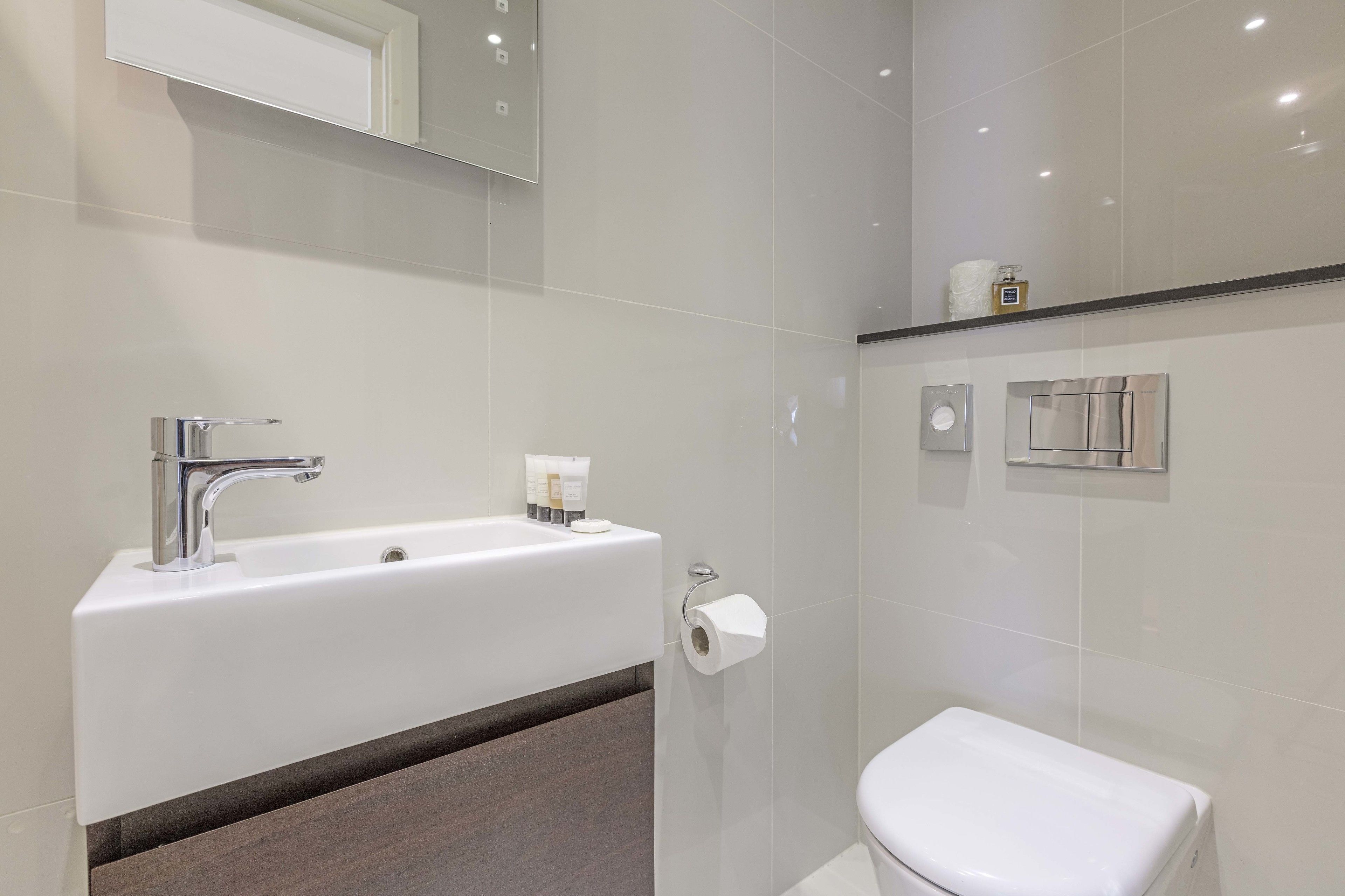 A modern bathroom with a white sink, chrome faucet, and a toilet.