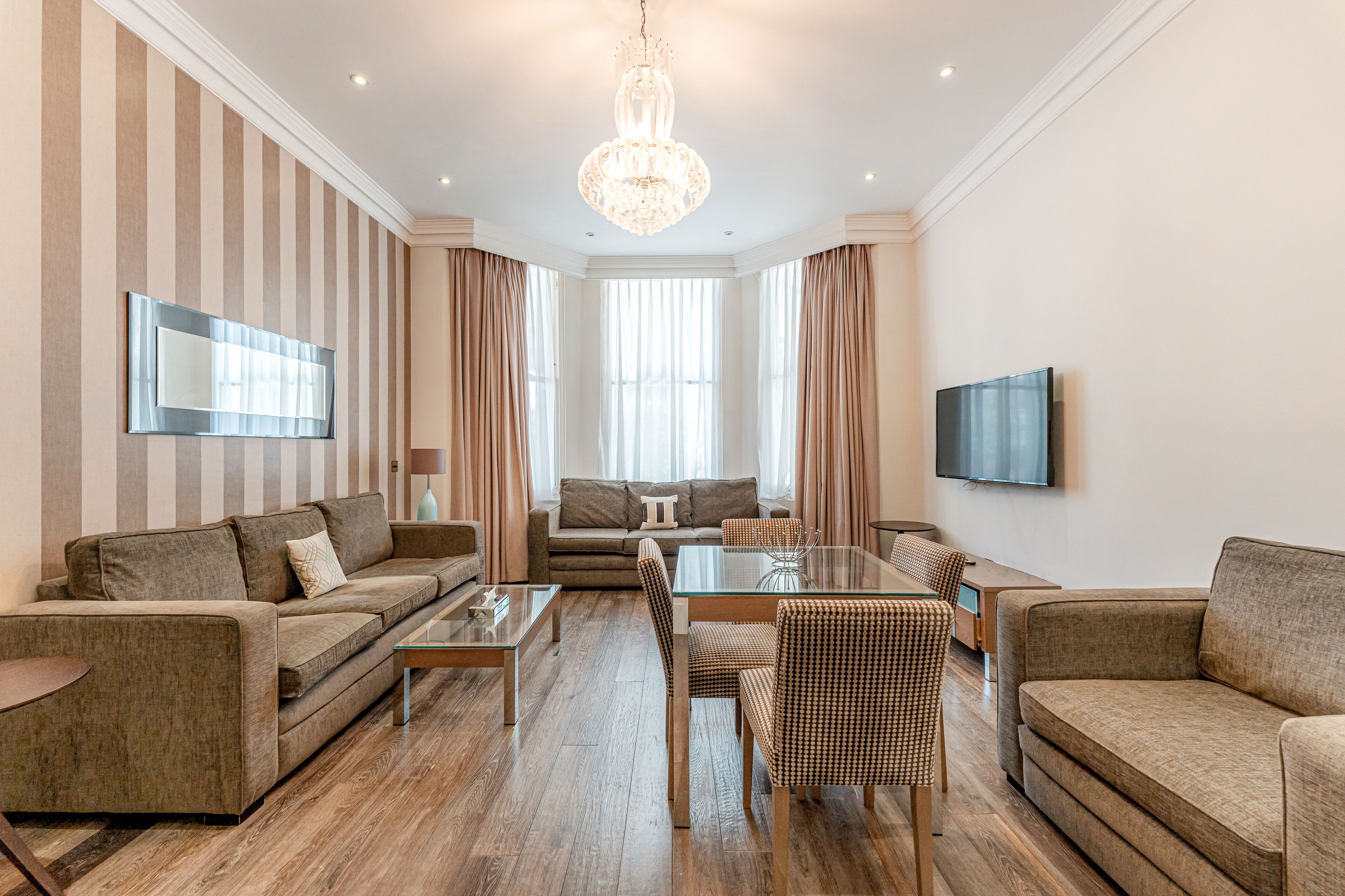 A modern living room with a sofa, armchairs, a glass coffee table, and a TV mounted on the wall.