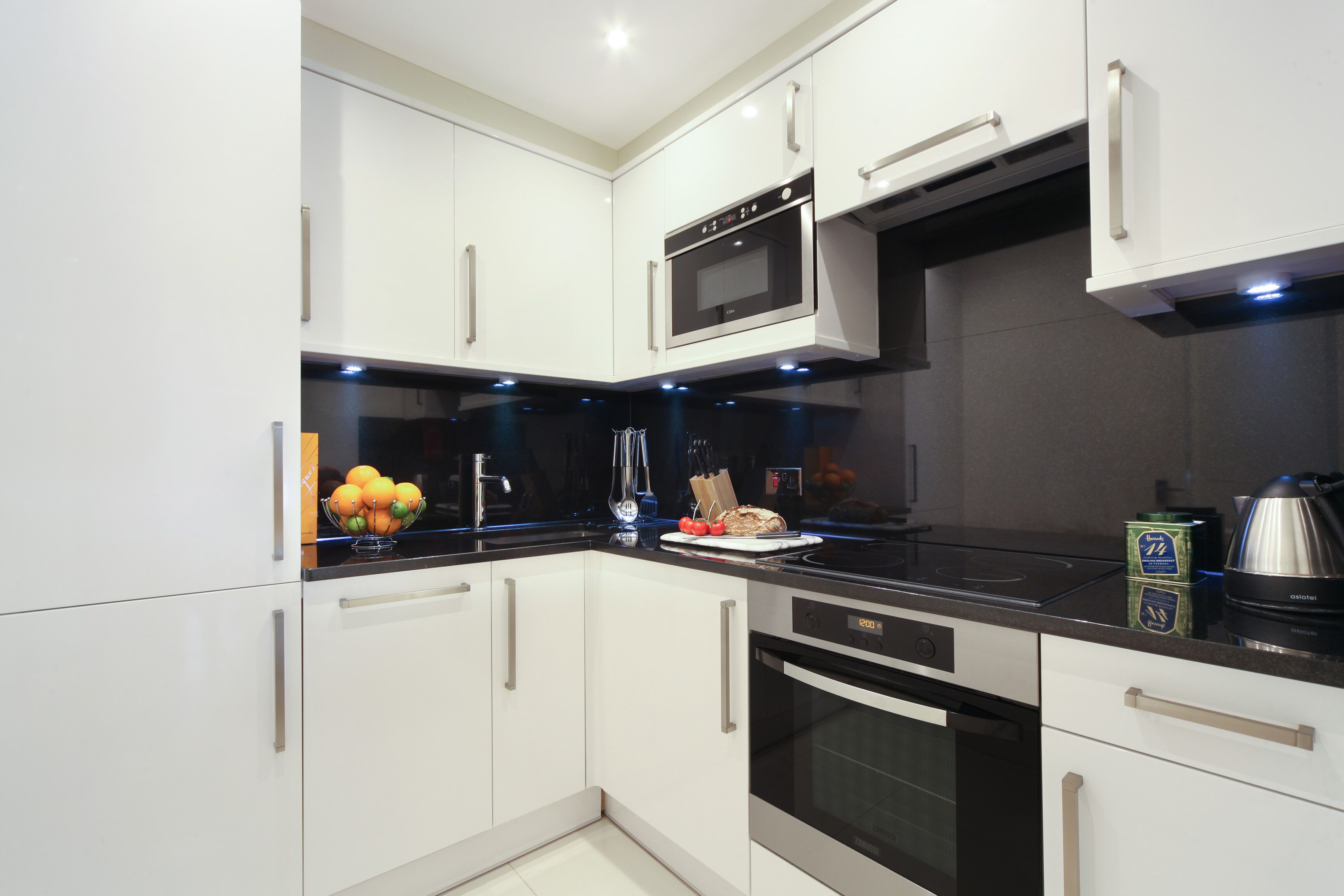 A modern kitchen with white cabinets, a black countertop, and stainless steel appliances including a microwave and oven.