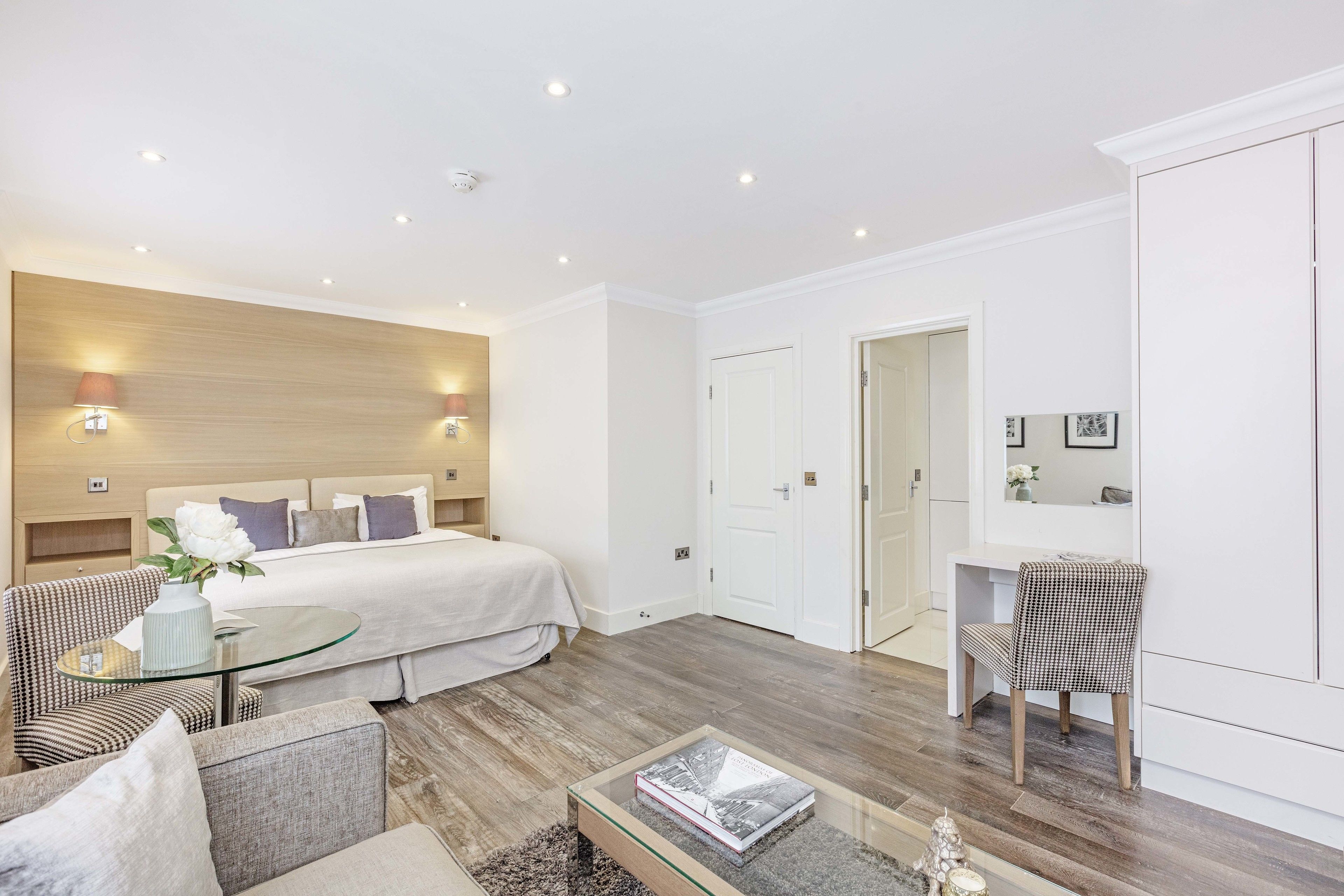Une chambre d’hôtel moderne comprenant un lit, une table basse en verre, un coin salon avec un fauteuil et un bureau avec une chaise.