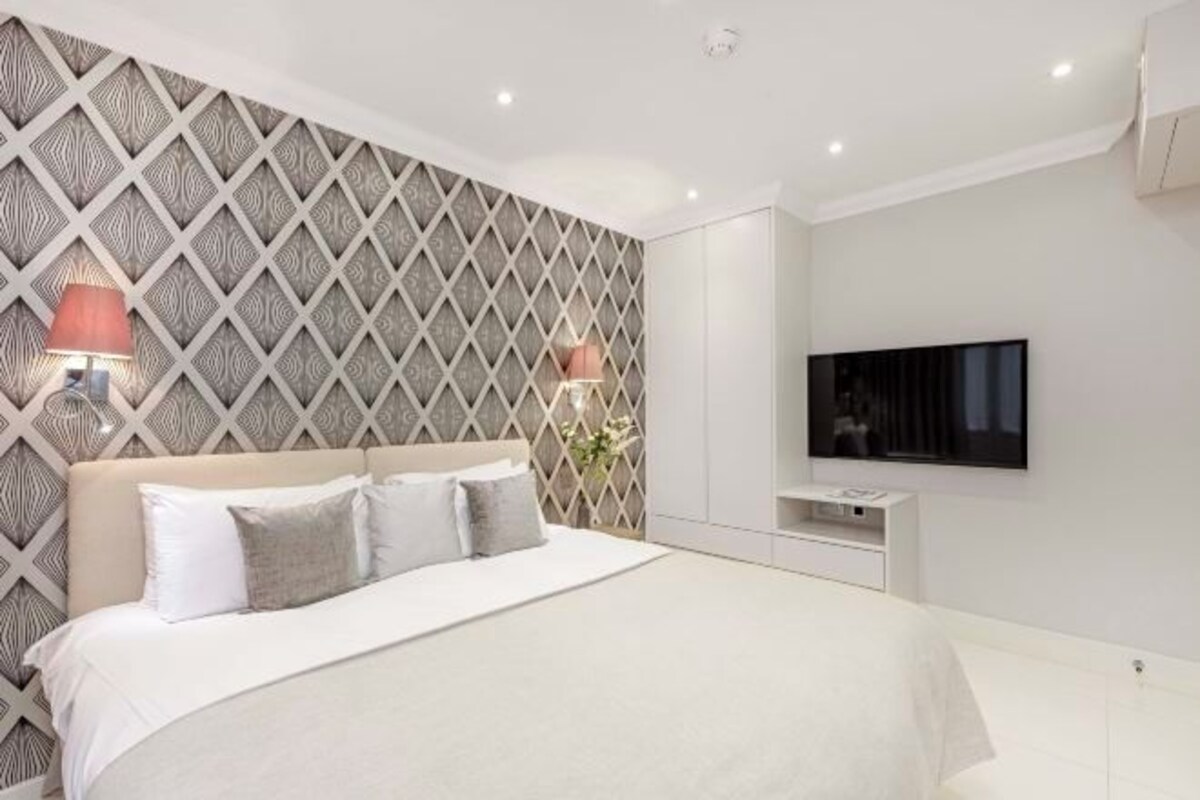 A modern bedroom with a large bed, a TV mounted on the wall, and a patterned wall design.