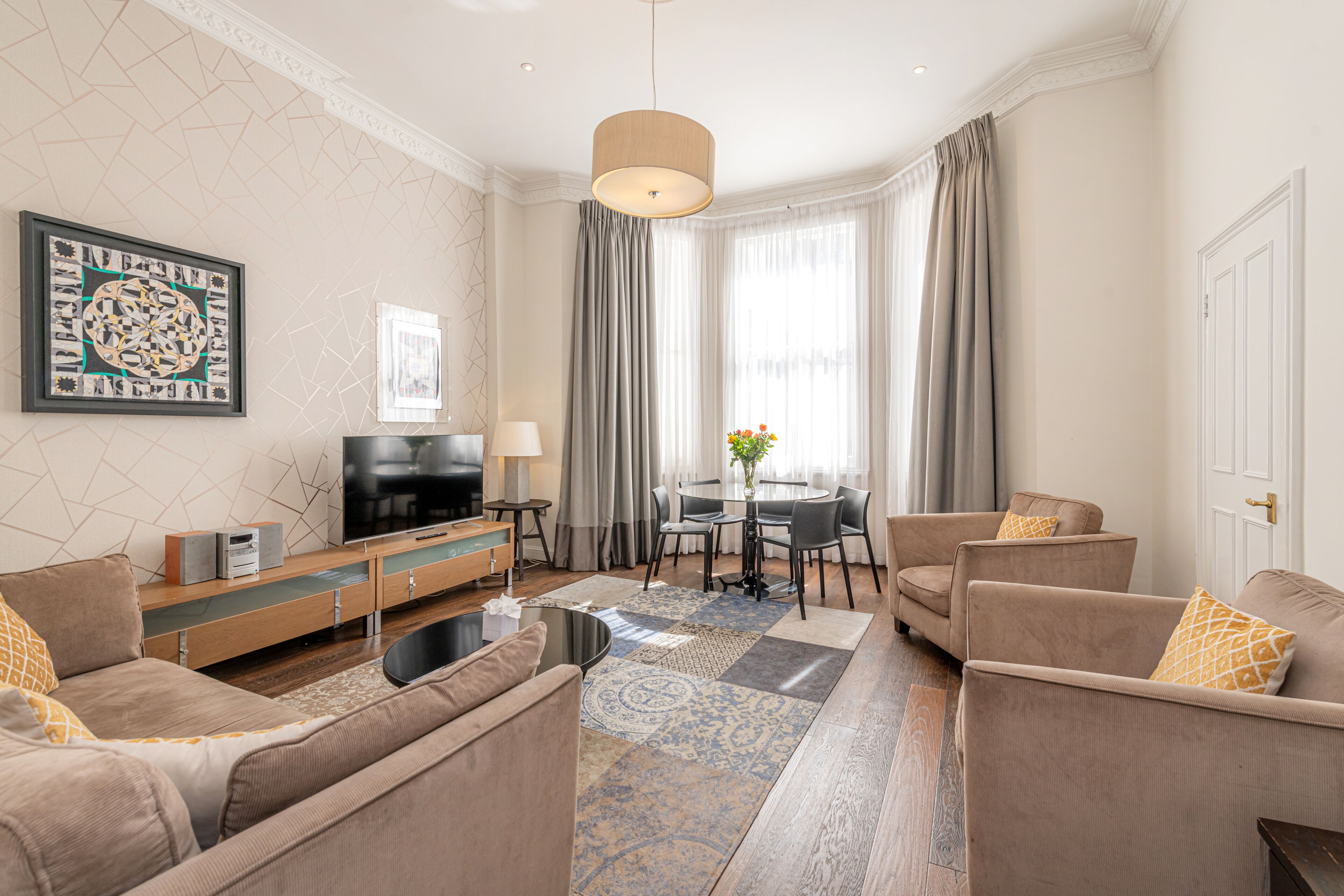 A modern living room with a flat-screen TV, sofas, a coffee table, and a dining area with a table and chairs.