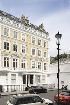 Un immeuble à plusieurs étages, de style architectural classique, caractérisé par un parement en briques blanches et jaunes, de grandes fenêtres et un lampadaire noir bien visible.