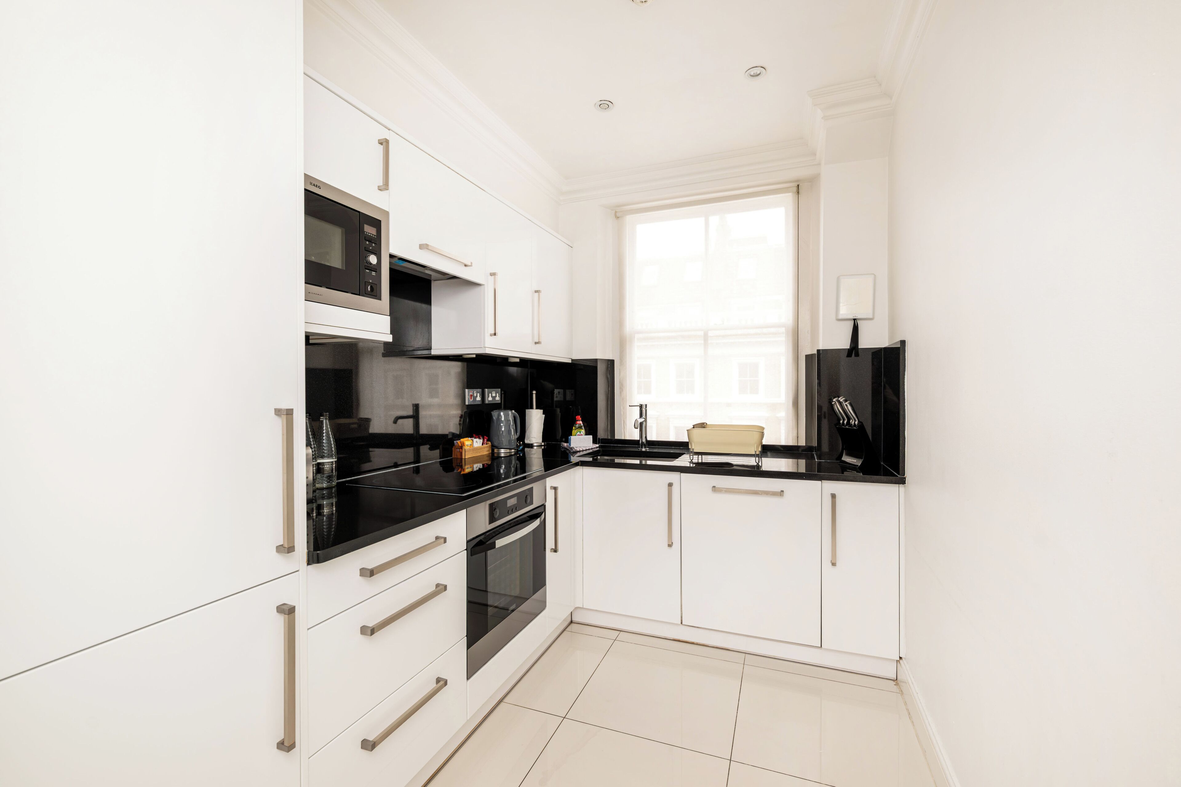 A modern kitchen with white cabinetry, a black countertop, and a window providing natural light.