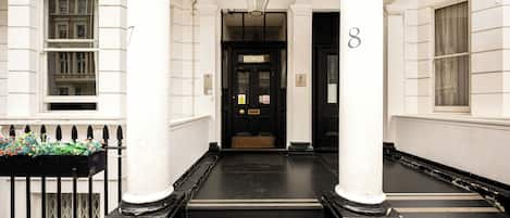 A building entrance with a black and white facade, numbered doors, and a black metal gate with flowers.
