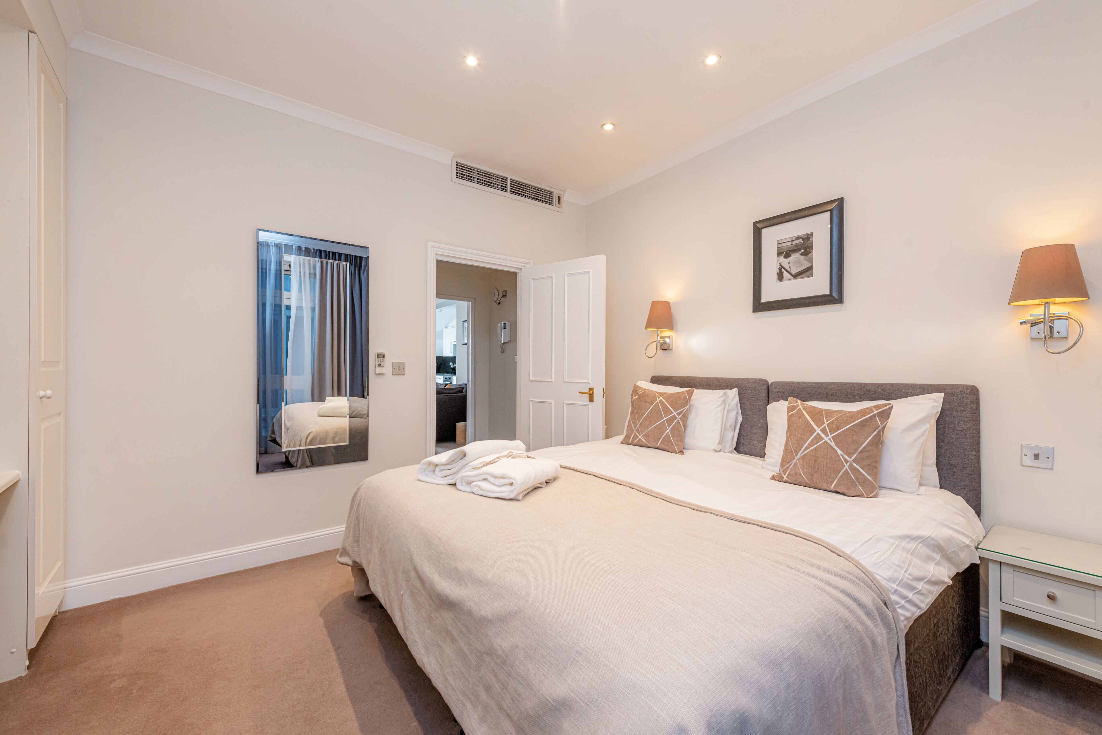 A bedroom with a large bed, a bedside table, a mirror, and a framed picture on the wall.