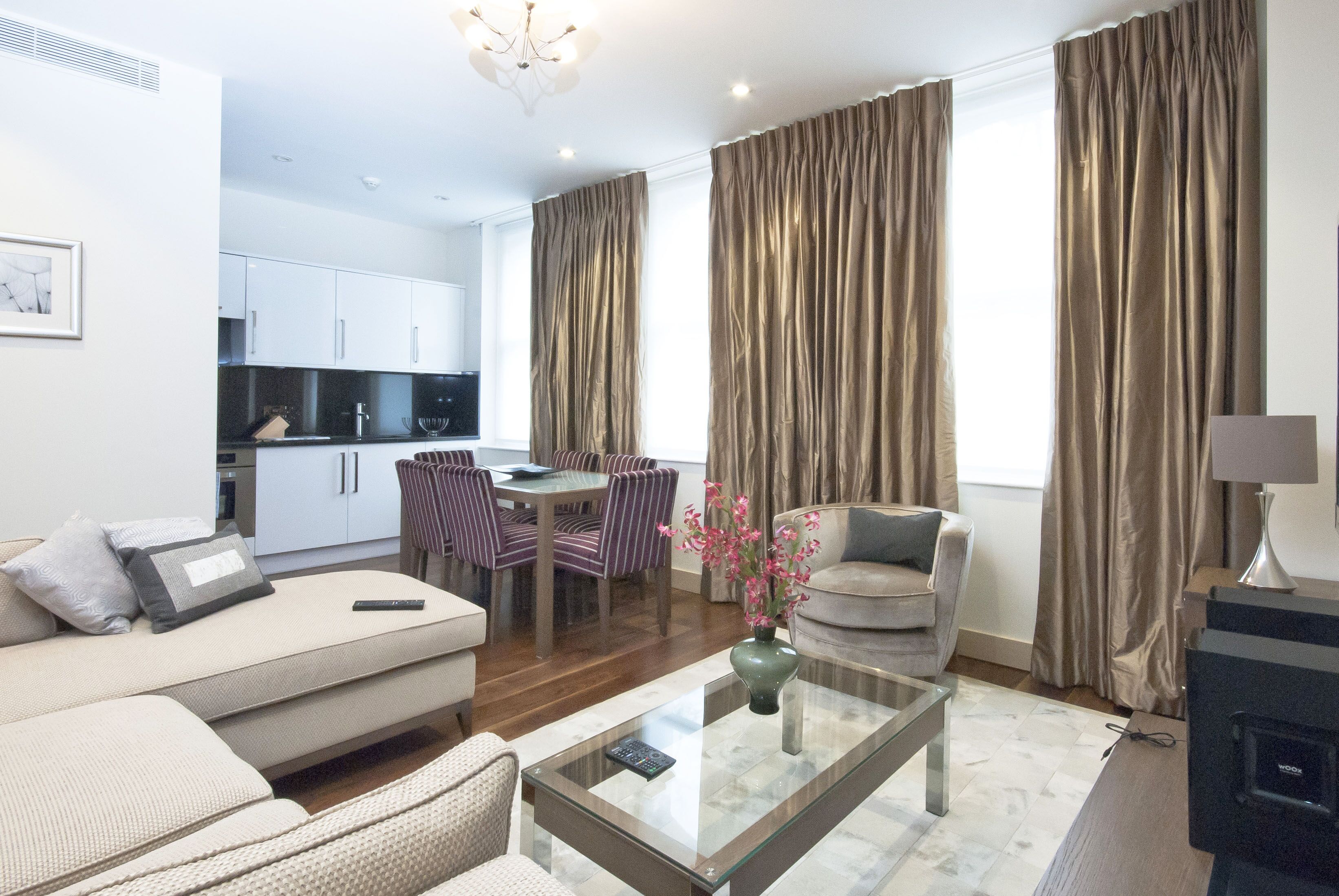 A modern living room with a sofa, a glass coffee table, and a dining area with striped chairs.