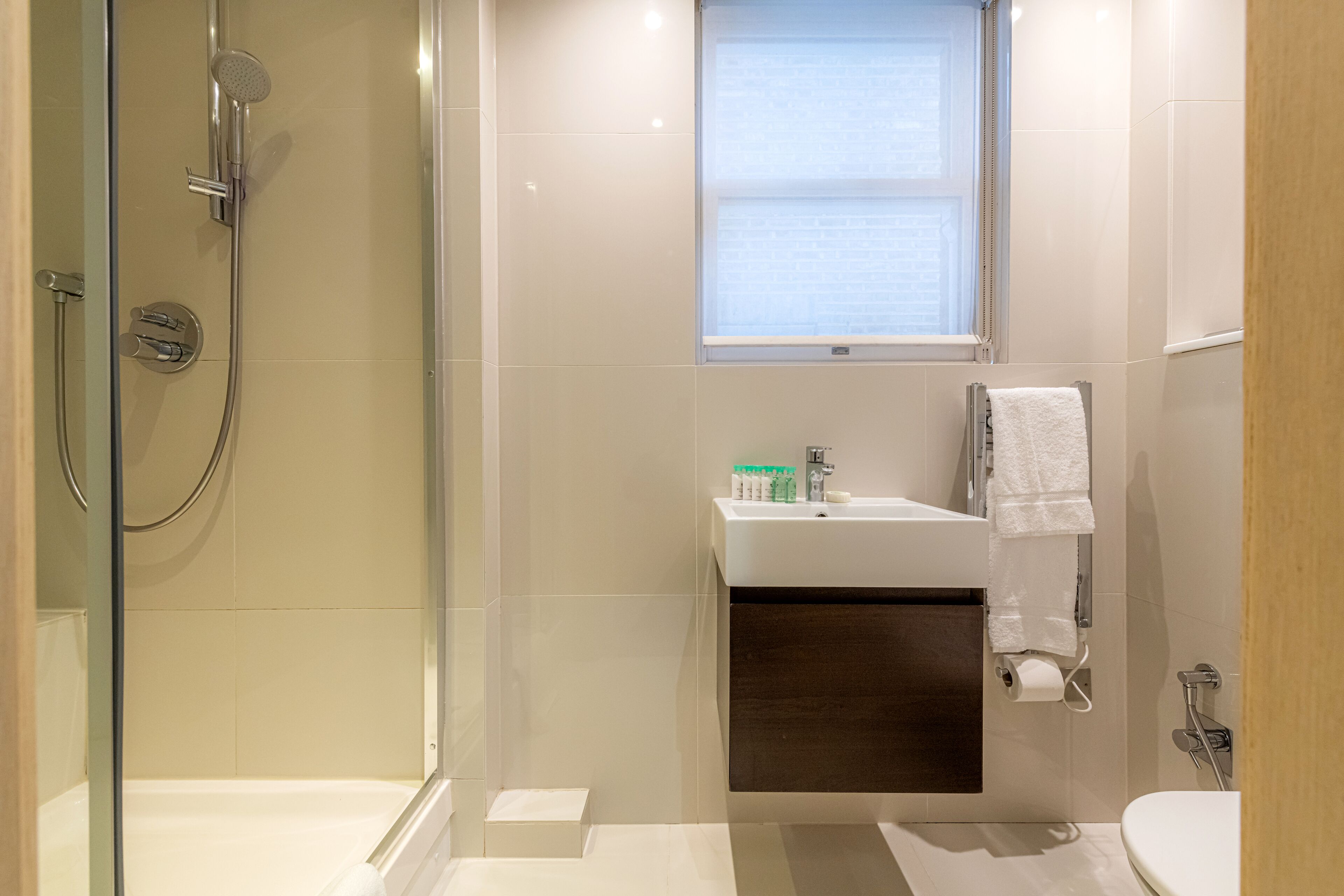 A modern bathroom with a glass-enclosed shower, a sink with toiletries, and a toilet.