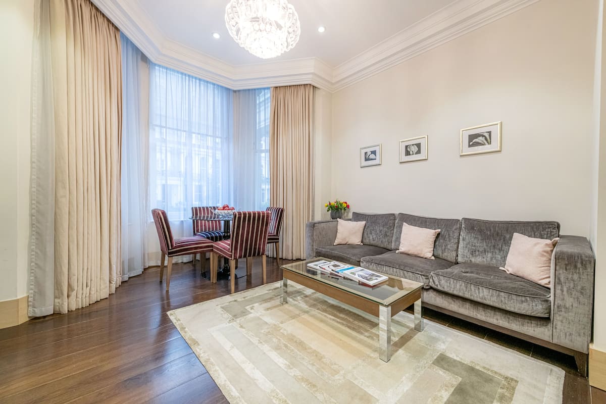 A living room with a grey sofa, a glass coffee table, striped chairs, and a dining table with chairs.