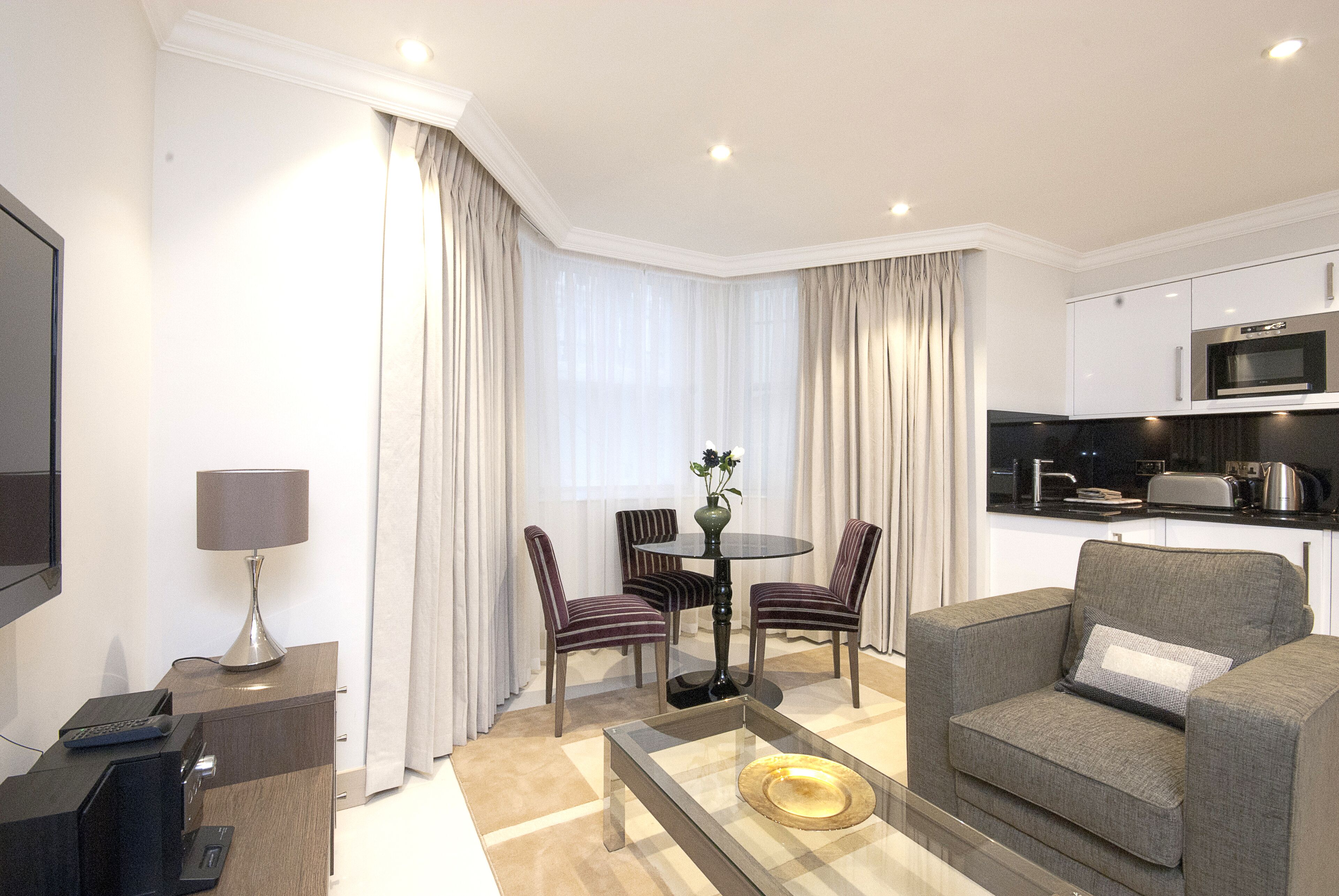 Ein modernes Hotelzimmer mit Sitzecke, Esstisch, einer Couch, einem Fernseher und einer Küchenzeile.