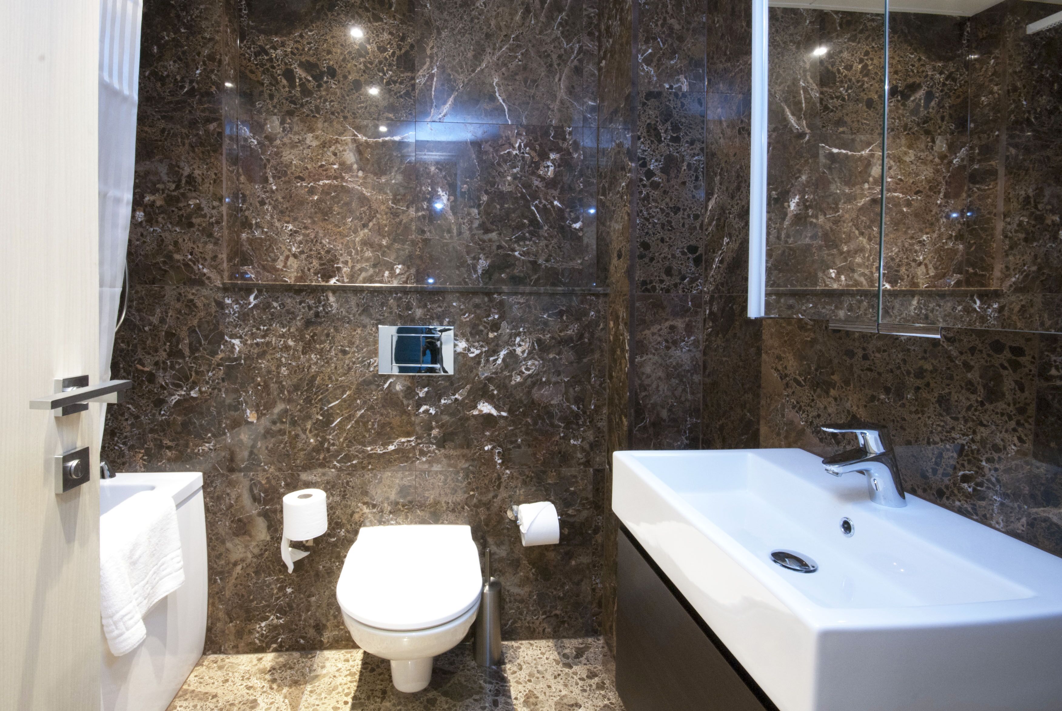 Une salle de bain moderne avec un mur en marbre, des toilettes, un lavabo et un miroir.