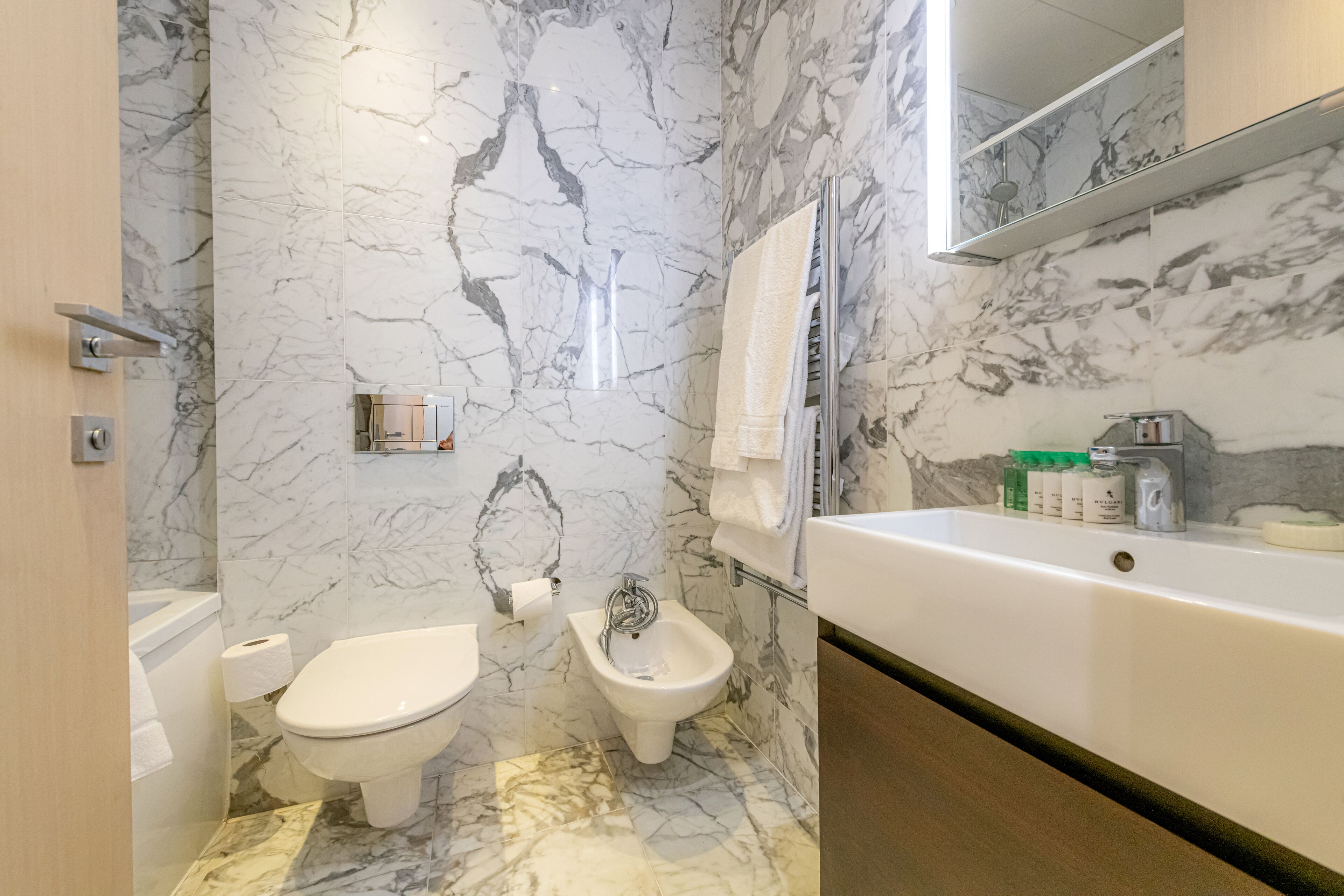 A bathroom with a toilet, bidet, and bathtub, all with marble walls and floors.