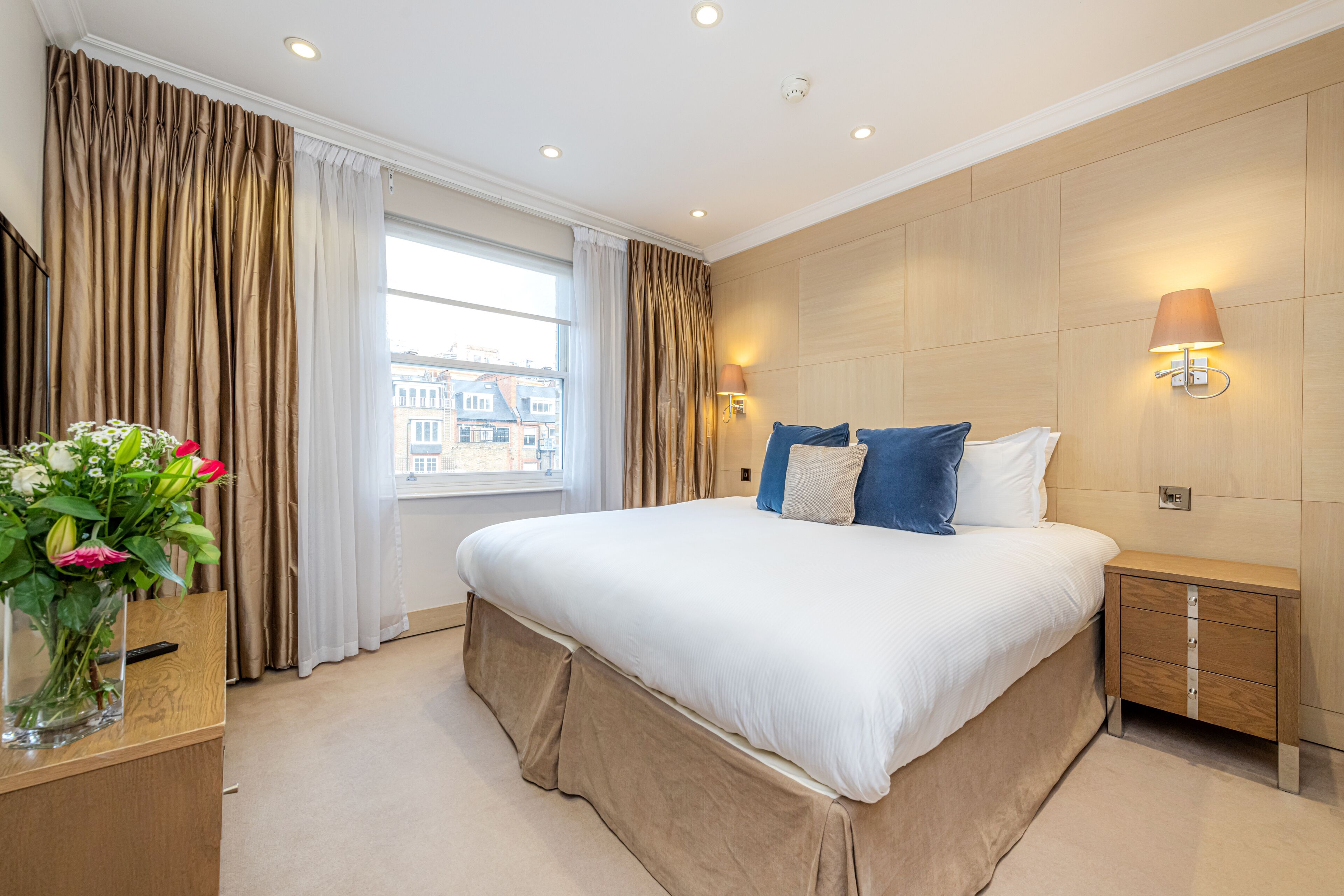 A hotel room with a large bed, a bedside table, a nightstand, a lamp, and a window with curtains.