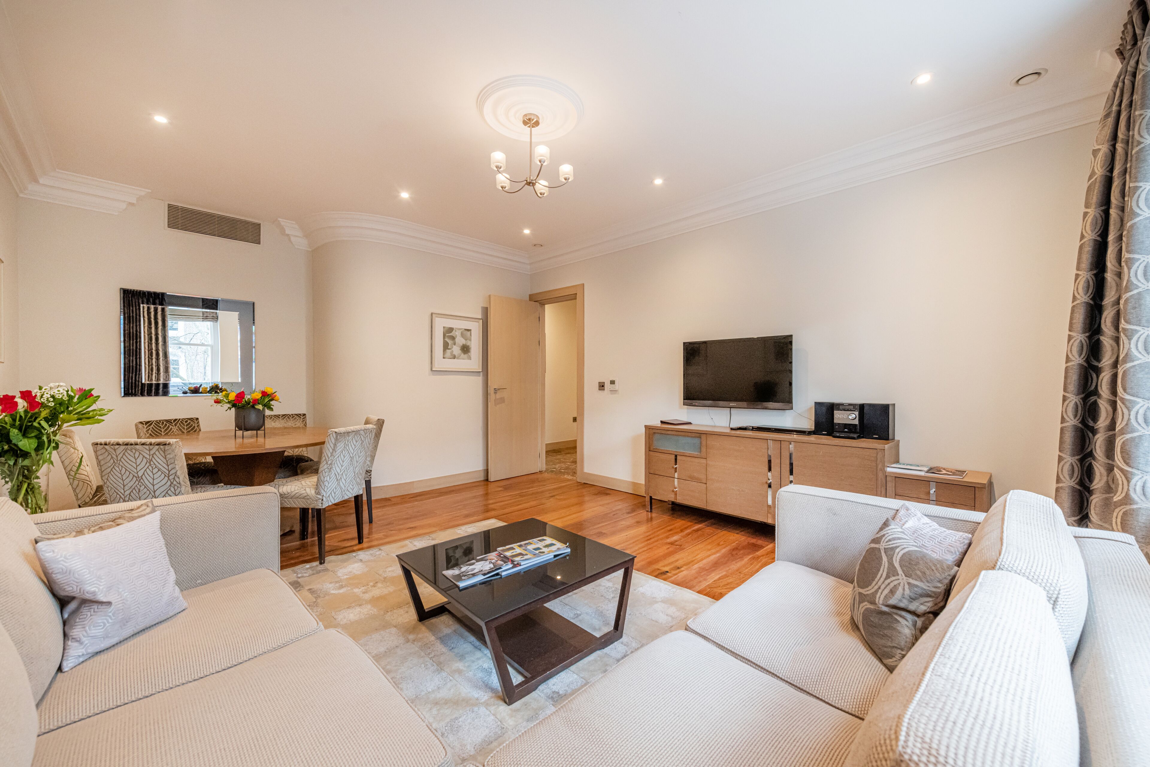 A modern living room with a sofa set, a coffee table, a TV, and a dining area with chairs and a table.
