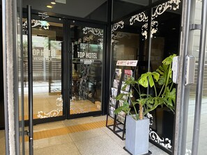 L’entrée d’un hôtel, avec des portes en verre, une enseigne indiquant « Top Hotel Residence », et une plante à l’extérieur.