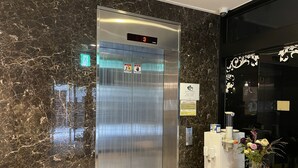Un ascensor con pantalla digital, señal de salida de emergencia y aviso de descuento por estancias superiores a 7 noches.