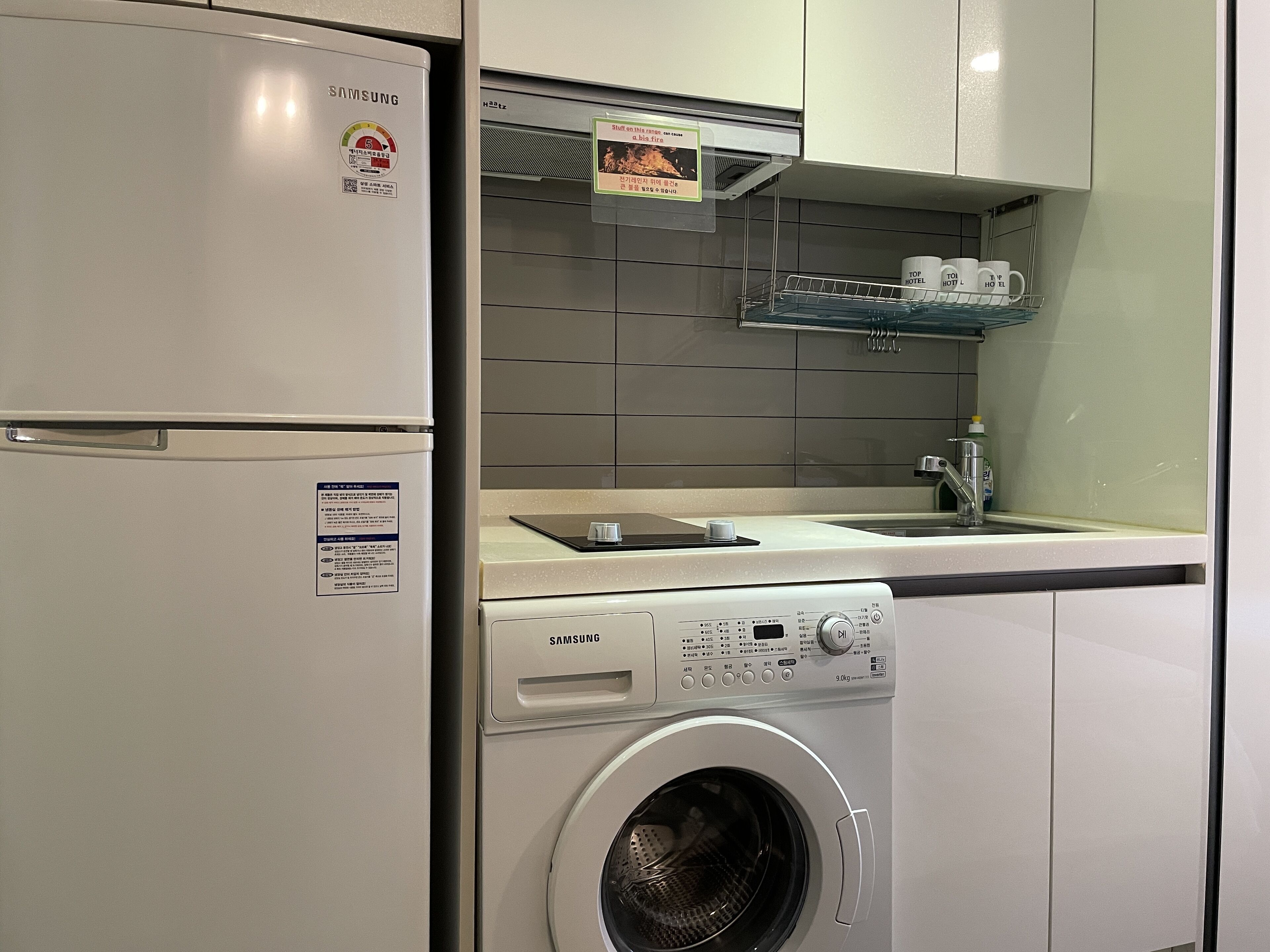Una cocina compacta con un refrigerador Samsung, lavadora integrada y un microondas.