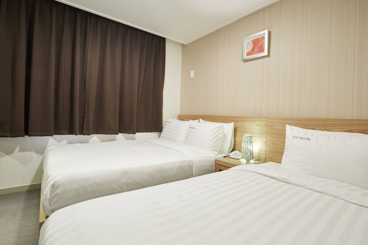 Habitación de hotel con dos camas, cabecero de madera, mesita de noche con teléfono y una obra de arte colgada en la pared.