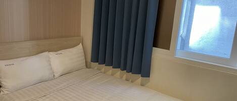 Une chambre d’hôtel avec un lit, deux oreillers, une fenêtre avec des rideaux et un interrupteur fixé au mur.