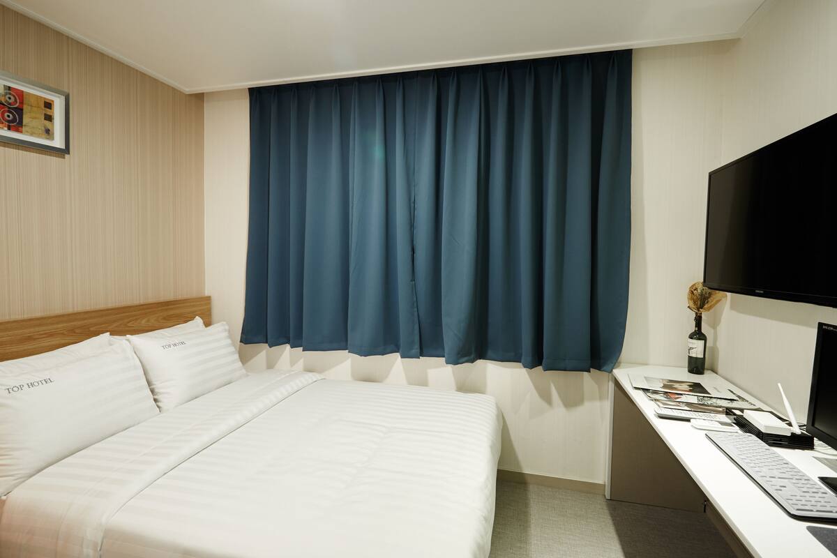 Una habitación de hotel con una cama, un escritorio con computadora, un televisor y una ventana con cortinas.