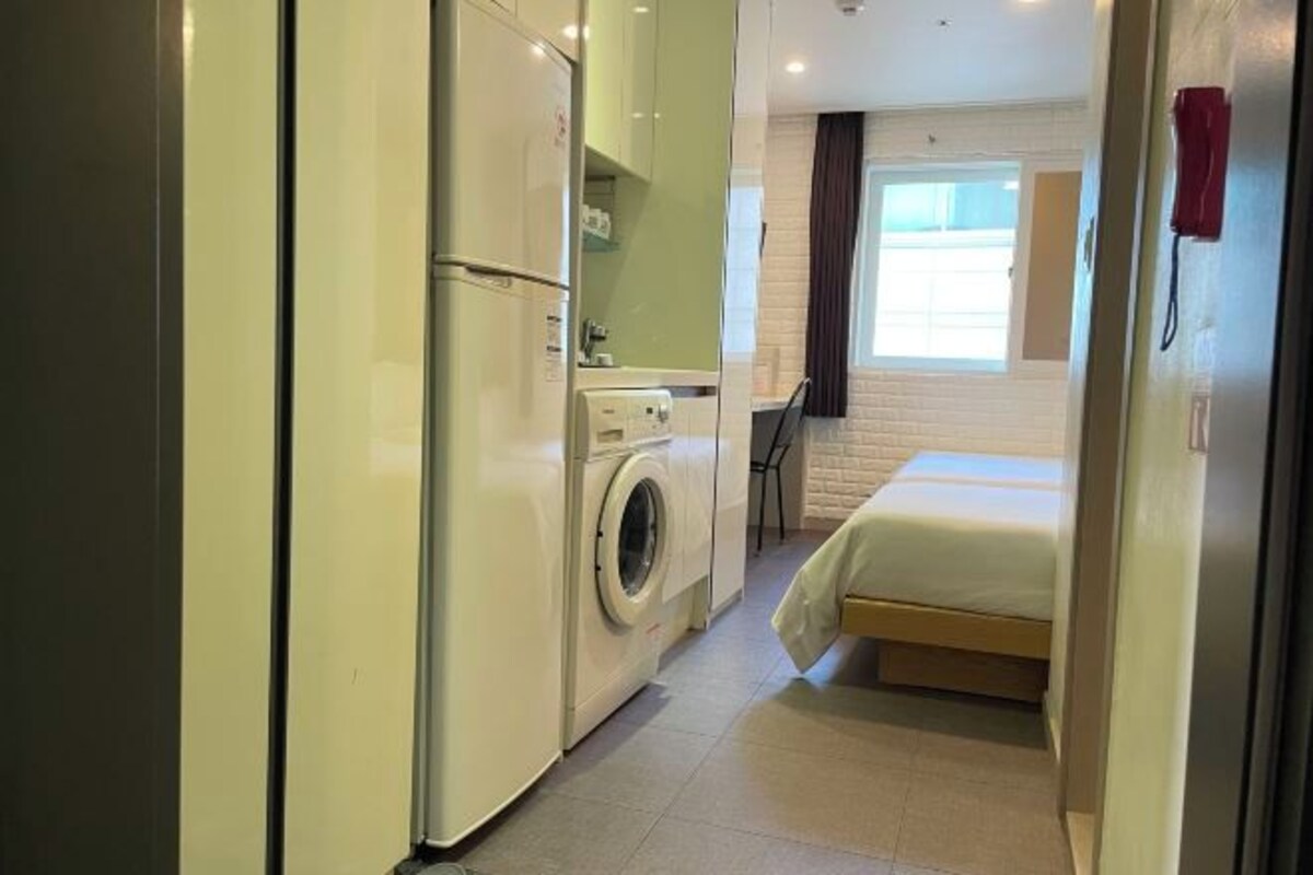 Een kleine hotelkamer met een wasmachine, een bed en een tafeltje.