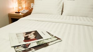 Una cama bien hecha con ropa de cama y almohadas blancas con la etiqueta "TOP HOTEL", una lámpara de noche y una revista sobre la cama.