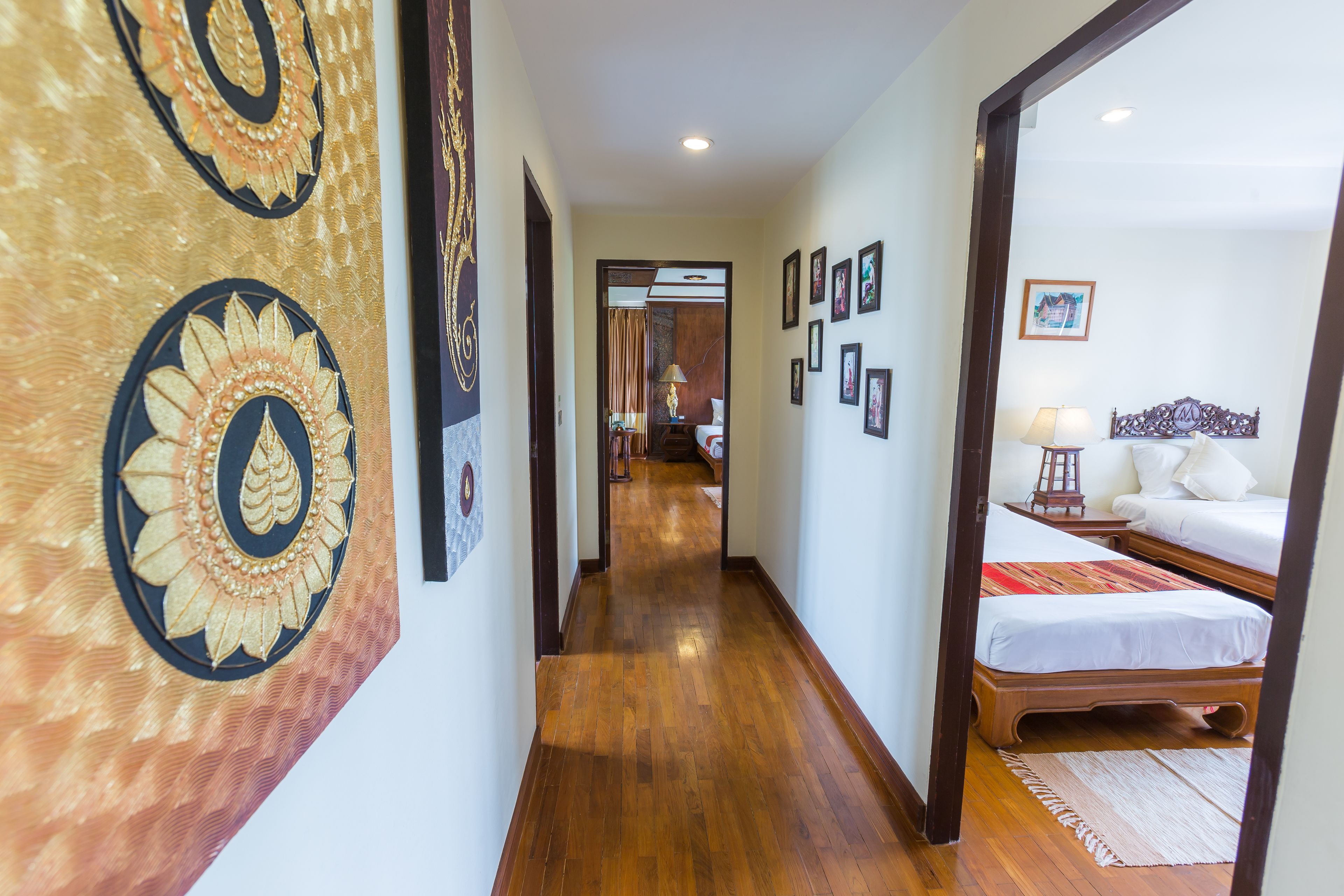 Un pasillo con suelo de madera, una cama con manta roja y una pared con cuadros enmarcados.